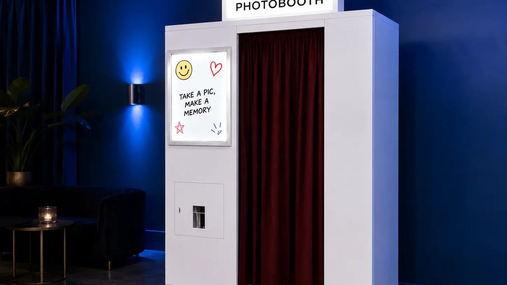 A photo booth placed against the wall of a dark lounge, lit from the topper